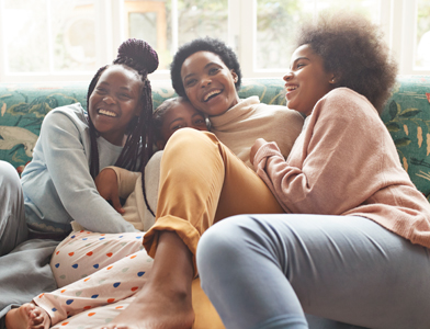 mother and 3 daughters laughing and cuddling on sofa